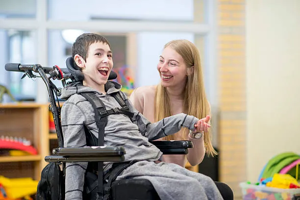 A support worker sharing a joyful moment with a young client in his wheelchair