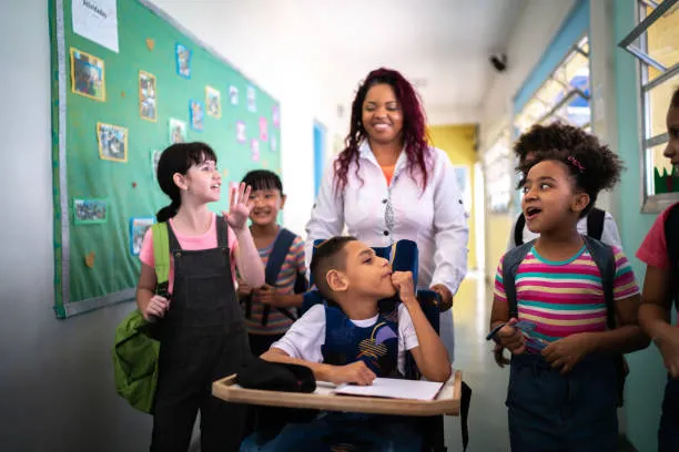 A teacher and a group of smiling children, including a boy in a wheelchair, in a school hallway